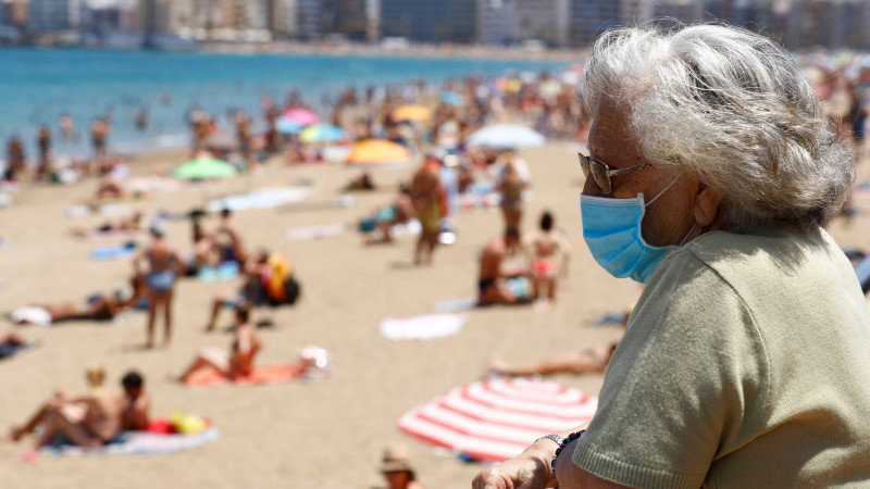 A woman wearing a face mask watches people sunbathing on the Las Canteras beach as some Spanish provinces are allowed to ease lockdown restrictions during phase two, amid the coronavirus disease (COVID-19) outbreak, in Las Palmas de Gran Canaria, the island of Gran Canaria, Spain May 31, 2020. REUTERS/Borja Suarez