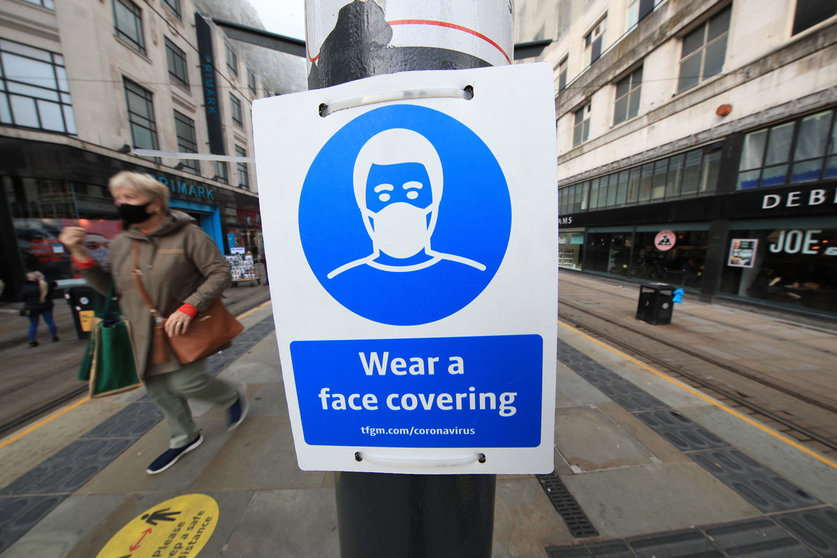 09 October 2020, England, Manchester: A woman wears a face mask passes by a sign advising on wearing face coverings near a tram stop. Cities in northern England and other areas suffering a surge in Covid-19 cases which that made many pubs and restaurants temporarily closed to combat the spread of the virus. Photo: Danny Lawson/dpa.