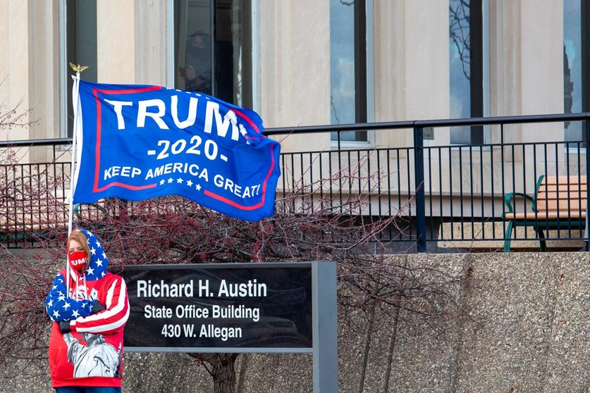 23 November 2020, US, Lansing: A supporter of US President Donald Trump waves a flag outside the Michigan Secretary of State office during the Michigan Board of State Canvassers meeting. The board subsequently certified the results of the 2020 presidential election, which showed Joe Biden ahead of President Trump by about 150,000 votes. Photo: Jim West/ZUMA Wire/dpa.