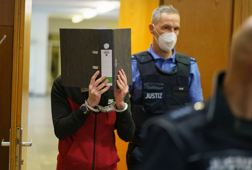 30 November 2021, Hessen, Frankfurt_Main: Iraqi defendant Taha Al-J. (L) coveres his face with a folder as he enters the courtroom of the Frankfurt's Higher Regional Court before a verdict is pronounced. The Federal Prosecution has accused Taha of genocide, crimes against humanity, war crimes, human trafficking and murder. As a suspected member of the so-called Islamic State (IS) terro group, he allegedly enslaved a Yazidi woman and her daughter and subjected them to abuse. According to the indictment, Taha faces accusations of leaving the little girl to die of thirst after tying her up in Fallujah, Iraq. Photo: Frank Rumpenhorst/dpa.